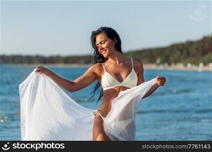 people, summer and swimwear concept - happy smiling young woman in bikini swimsuit with pareo posing on beach. woman in bikini swimsuit with pareo on beach