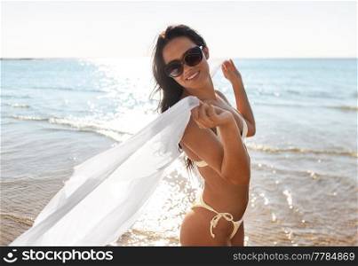 people, summer and swimwear concept - happy smiling young woman in bikini swimsuit with cover-up on beach. woman in bikini swimsuit with cover-up on beach