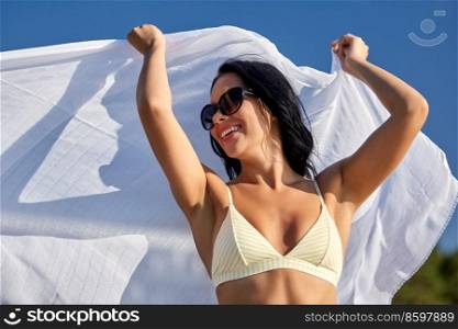 people, summer and swimwear concept - happy smiling young woman in bikini swimsuit with cover-up over blue sky. woman in bikini swimsuit with cover-up over sky
