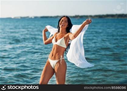 people, summer and swimwear concept - happy smiling young woman in bikini swimsuit with pareo on beach. woman in bikini swimsuit with pareo on beach