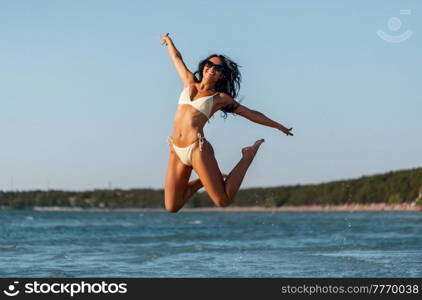 people, summer and swimwear concept - happy smiling young woman in bikini swimsuit jumping on beach. smiling young woman in bikini swimsuit on beach