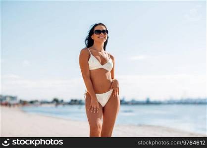 people, summer and swimwear concept - happy smiling young woman in bikini swimsuit on beach. smiling young woman in bikini swimsuit on beach