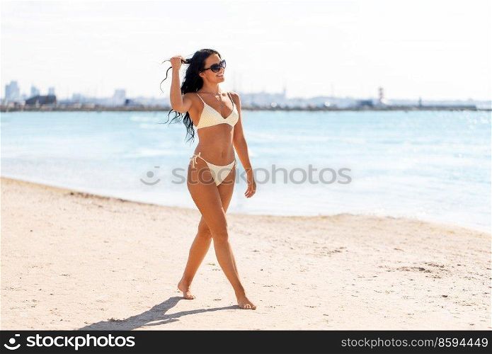 people, summer and swimwear concept - happy smiling young woman in bikini swimsuit walking along beach. smiling young woman in bikini swimsuit on beach