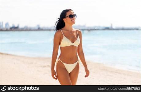 people, summer and swimwear concept - happy smiling young woman in bikini swimsuit walking along beach. smiling young woman in bikini swimsuit on beach