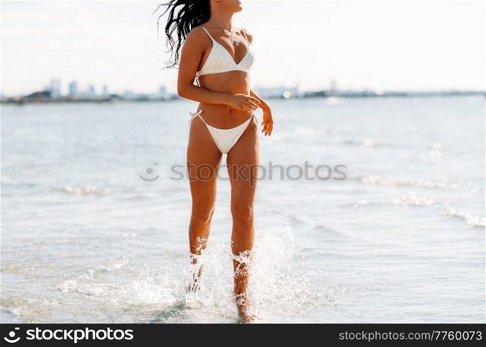 people, summer and swimwear concept - happy young woman in bikini swimsuit running in water beach. young woman in bikini swimsuit on beach