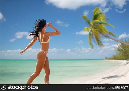 people, summer and swimwear concept - young woman in bikini swimsuit running in shallow water over tropical beach background in french polynesia. young woman in bikini swimsuit running on beach