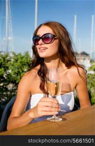 people, summer, drinks and holidays concept - smiling young woman wearing sunglasses drinking champagne on terrace