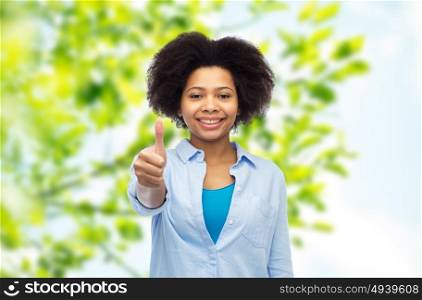 people, , summer, eco and gesture concept - happy afro american young woman showing thumbs up over green natural background. happy afro american woman showing thumbs up