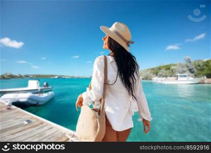 people, summer holidays and leisure concept - happy young woman in white shirt and straw hat with bag over pier and boat or tropical sea background in french polynesia. happy woman with bag on pier in summer