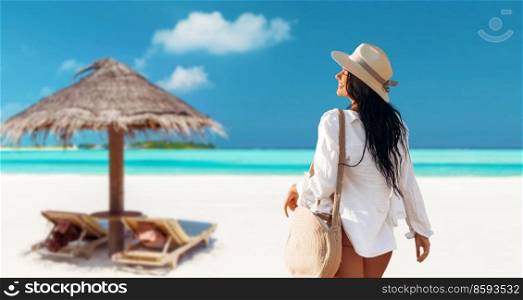 people, summer holidays and leisure concept - happy young woman in white shirt and straw hat with bag walking along beach. happy woman with bag walking along summer beach