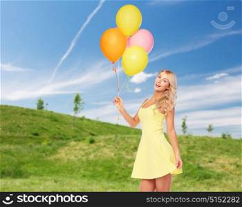 people, summer holidays and party concept - happy young woman or teen girl in pink dress with helium air balloons over blue sky and green field background. happy woman with helium air balloons in summer