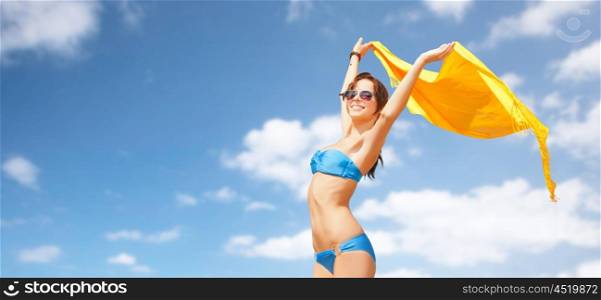people, summer holidays and vacation concept - beautiful woman in bikini and sunglasses with pareo over blue sky and clouds background