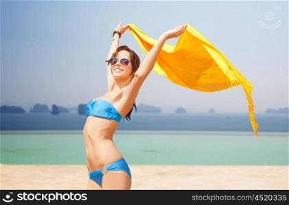 people, summer holidays and vacation concept - beautiful woman in bikini and sunglasses with pareo over over infinity edge pool and ocean background