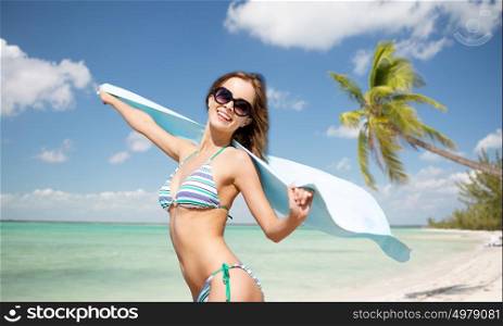 people, summer holidays and vacation concept - beautiful woman in bikini and sunglasses with towel over exotic tropical beach with palm trees background. woman in bikini and sunglasses with towel on beach