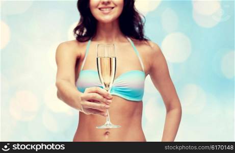people, summer holidays, celebration, drinks and beach concept - happy young woman in bikini swimsuit drinking champagne at party over blue holidays lights background