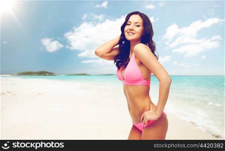 people, summer holidays, travel and tourism concept - happy young woman posing in pink bikini swimsuit over exotic tropical beach background