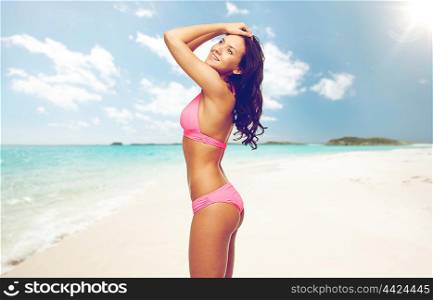 people, summer holidays, travel and tourism concept - happy young woman posing in pink bikini swimsuit over exotic tropical beach background