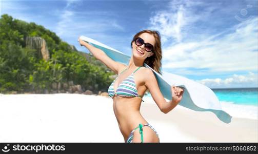 people, summer holidays, travel and vacation concept - happy smiling woman in bikini and sunglasses with pareo posing over exotic tropical beach background. woman in bikini and sunglasses with pareo on beach