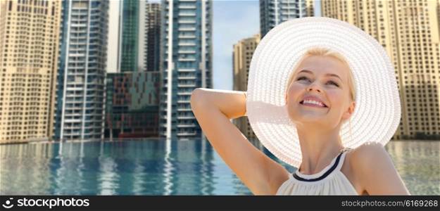 people, summer holidays, travel, tourism and vacation concept - beautiful woman in sun hat enjoying summer over dubai city and infinity edge pool background