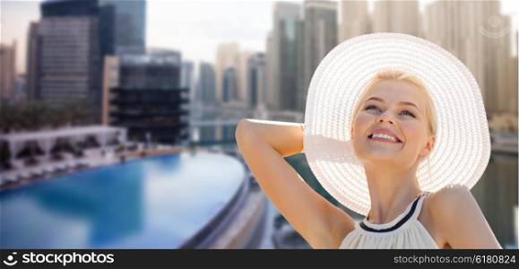 people, summer holidays, travel, tourism and vacation concept - beautiful woman in sun hat enjoying summer over dubai city background