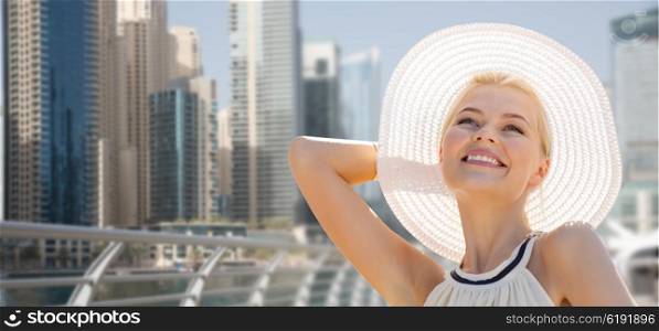 people, summer holidays, travel, tourism and vacation concept - happy beautiful woman in sun hat enjoying summer over dubai city waterfront background