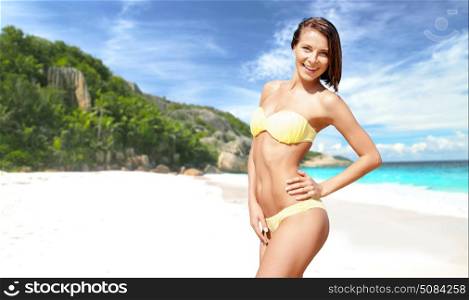 people, summer holidays, vacation and travel concept - happy smiling young woman posing in bikini swimsuit posing over exotic tropical beach and sea shore background. happy woman in bikini swimsuit on tropical beach. happy woman in bikini swimsuit on tropical beach