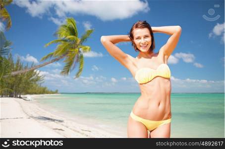 people, summer holidays, vacation and travel concept - happy young woman posing in bikini swimsuit with raised hands over exotic tropical beach with palm trees and sea shore background. happy woman in bikini swimsuit on tropical beach