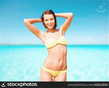 people, summer holidays, vacation and travel concept - happy young woman posing in bikini swimsuit with raised hands over blue sky and sea background. happy woman in bikini swimsuit over blue sea