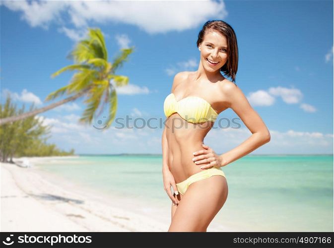people, summer holidays, vacation and travel concept - happy young woman posing in bikini swimsuit over exotic tropical beach with palm trees and sea shore background. happy woman in bikini swimsuit on tropical beach