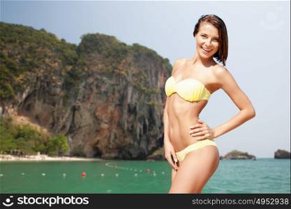 people, summer holidays, vacation and travel concept - happy young woman posing in bikini swimsuit over bali beach and rock background. happy woman in bikini swimsuit on bali beach