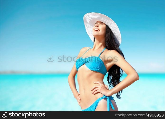 people, summer holidays, vacation and travel concept - happy young woman posing in bikini swimsuit and hat on beach over sea and blue sky background. happy woman in bikini swimsuit on tropical beach