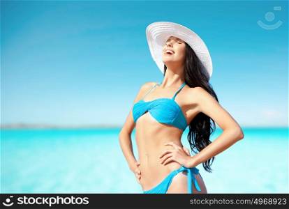 people, summer holidays, vacation and travel concept - happy young woman posing in bikini swimsuit and hat on beach over sea and blue sky background. happy woman in bikini swimsuit on tropical beach