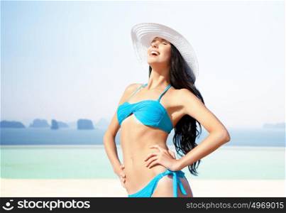 people, summer holidays, vacation and travel concept - happy young woman posing in bikini swimsuit and hat over sea and infinity edge pool background. happy woman in bikini swimsuit over edge pool