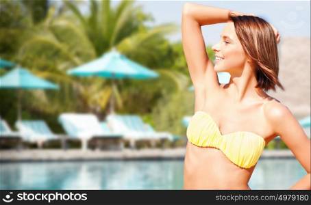people, summer holidays, vacation and travel concept - happy young woman posing in bikini swimsuit with raised hand over pool and palm trees background. happy woman in bikini swimsuit on tropical beach