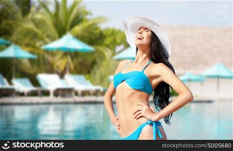people, summer holidays, vacation and travel concept - happy young woman posing in bikini swimsuit and hat over swimming pool background. happy woman in bikini swimsuit over swimming pool