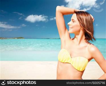 people, summer holidays, vacation and travel concept - happy young woman posing in bikini swimsuit with raised hand over exotic tropical beach background. happy woman in bikini swimsuit on tropical beach