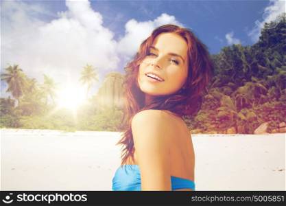 people, summer holidays, vacation and travel concept - happy young woman posing in bikini swimsuit with raised hands over exotic tropical beach with palm trees and sea shore background. happy woman in bikini swimsuit on tropical beach