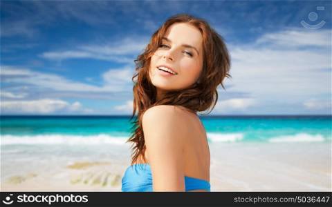 people, summer holidays, vacation and travel concept - happy young woman posing in bikini swimsuit with raised hands over exotic tropical beach and sea shore background. happy woman in bikini swimsuit on tropical beach