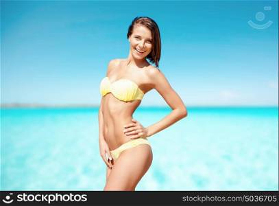 people, summer holidays, vacation and travel concept - happy young woman posing in bikini swimsuit on beach over sea and blue sky background. happy woman in bikini swimsuit on tropical beach