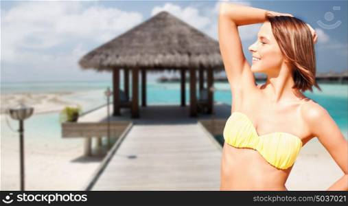 people, summer holidays, vacation and travel concept - happy young woman posing in bikini swimsuit with raised hand over exotic tropical beach background. happy woman in bikini swimsuit on tropical beach