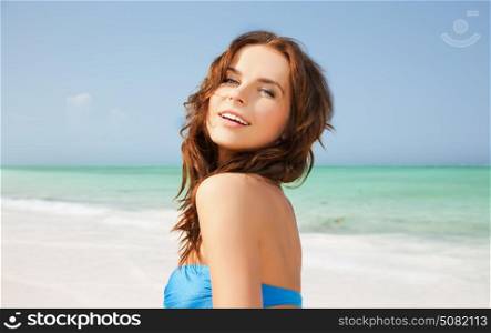 people, summer holidays, vacation and travel concept - happy young woman posing in bikini swimsuit with raised hands over exotic tropical beach and sea shore background. happy woman in bikini swimsuit on tropical beach
