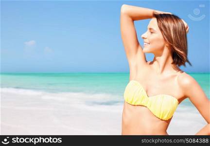people, summer holidays, vacation and travel concept - happy young woman posing in bikini swimsuit with raised hand over exotic tropical beach background. happy woman in bikini posing on summer beach. happy woman in bikini posing on summer beach