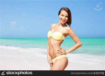 people, summer holidays, vacation and travel concept - happy young woman posing in bikini swimsuit over exotic tropical beach background. happy woman in bikini posing on summer beach