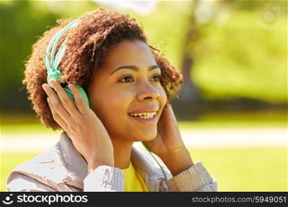 people, summer, technology and leisure concept - happy african american young woman face with headphones listening to music outdoors