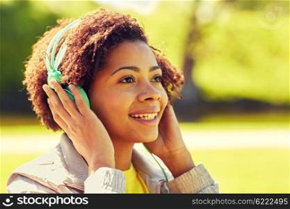 people, summer, technology and leisure concept - happy african american young woman face with headphones listening to music outdoors
