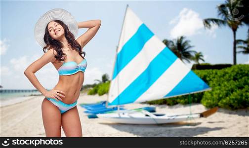 people, summer vacation, tourism and travel concept - happy young woman in bikini swimsuit and sun hat over sailing boats on tropical beach background