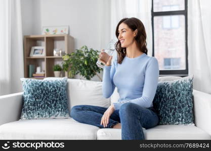 people, sustainability and leisure concept - happy smiling young woman drinking water from glass bottle at home. woman drinking water from glass bottle at home