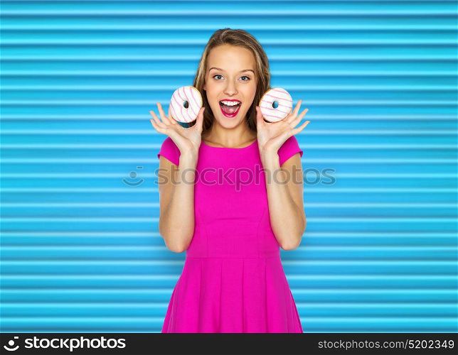 people, sweets and fast food concept - happy young woman or teen girl in pink dress with donuts over blue ribbed background. happy woman or teen girl with donuts