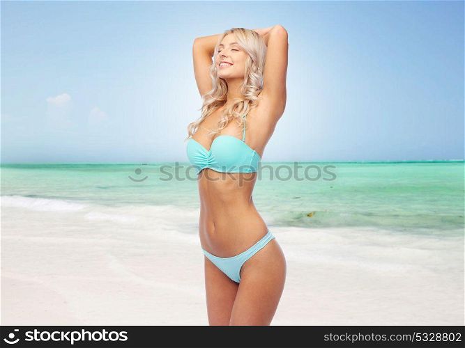 people, swimwear and summer concept - happy smiling young woman in bikini swimsuit over exotic tropical beach background. happy woman in bikini swimsuit on summer beach