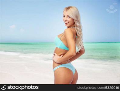 people, swimwear and summer concept - happy smiling young woman in bikini swimsuit over exotic tropical beach background. happy woman in bikini swimsuit on summer beach